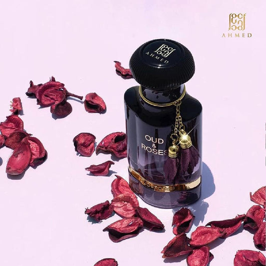Perfume bottle labeled 'Oud & Rose' by AHMED with dried rose petals on a light pink background